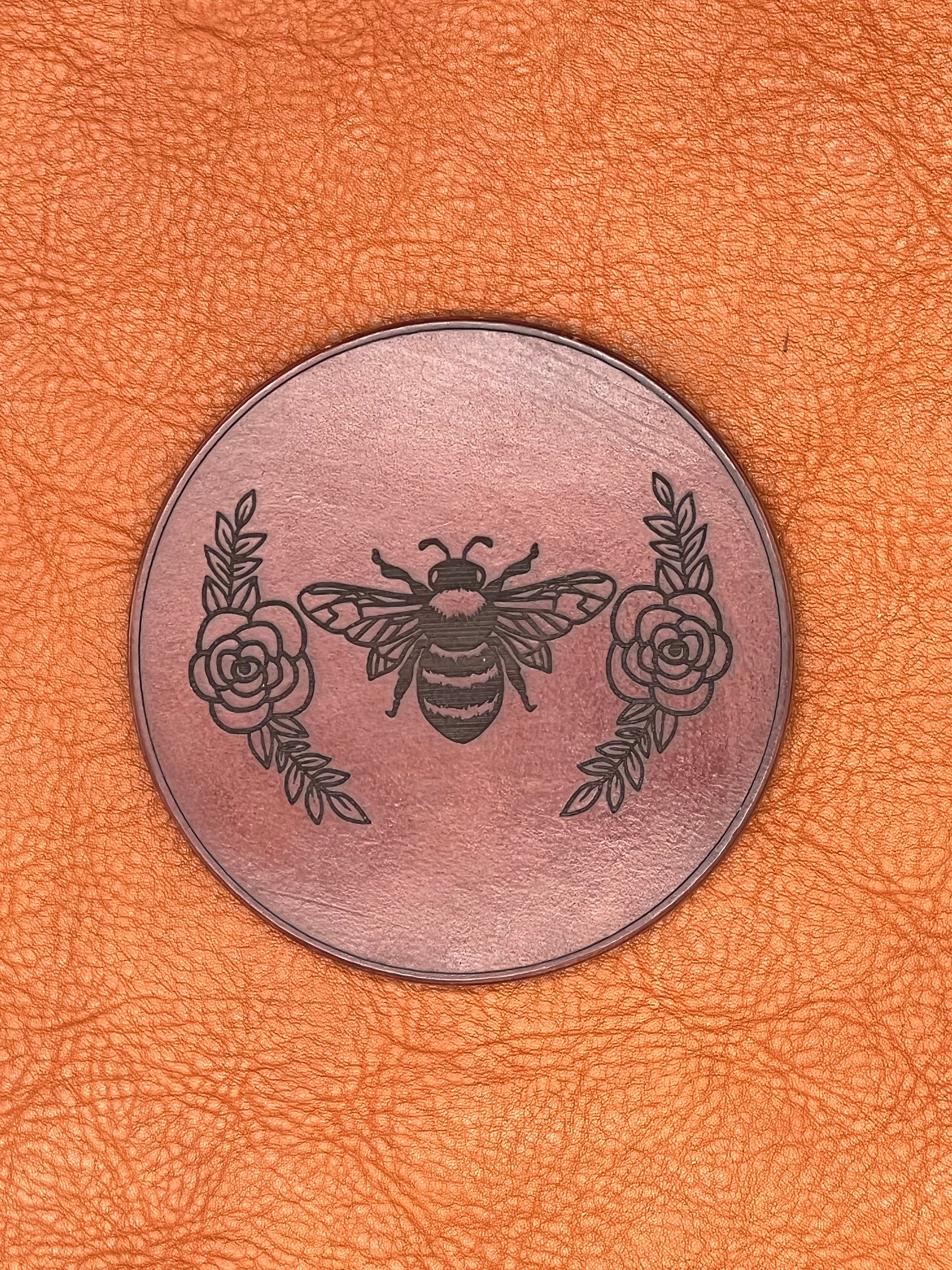 a chestnut colored leather coaster featuring an engraved bee flanked with roses