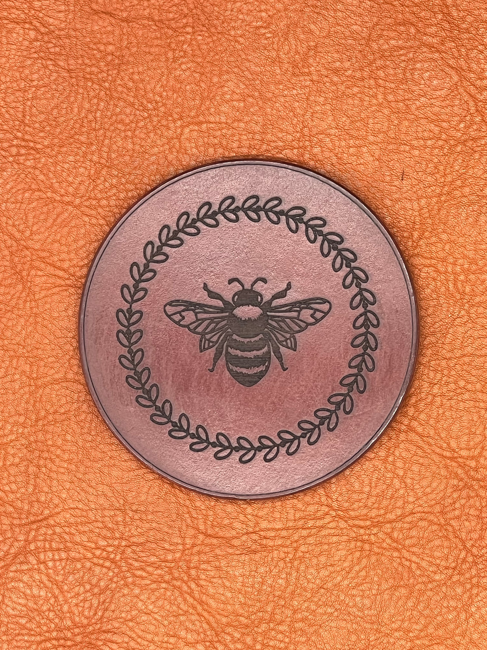 a chestnut colored leather coaster featuring an engraved bee encircled with vines