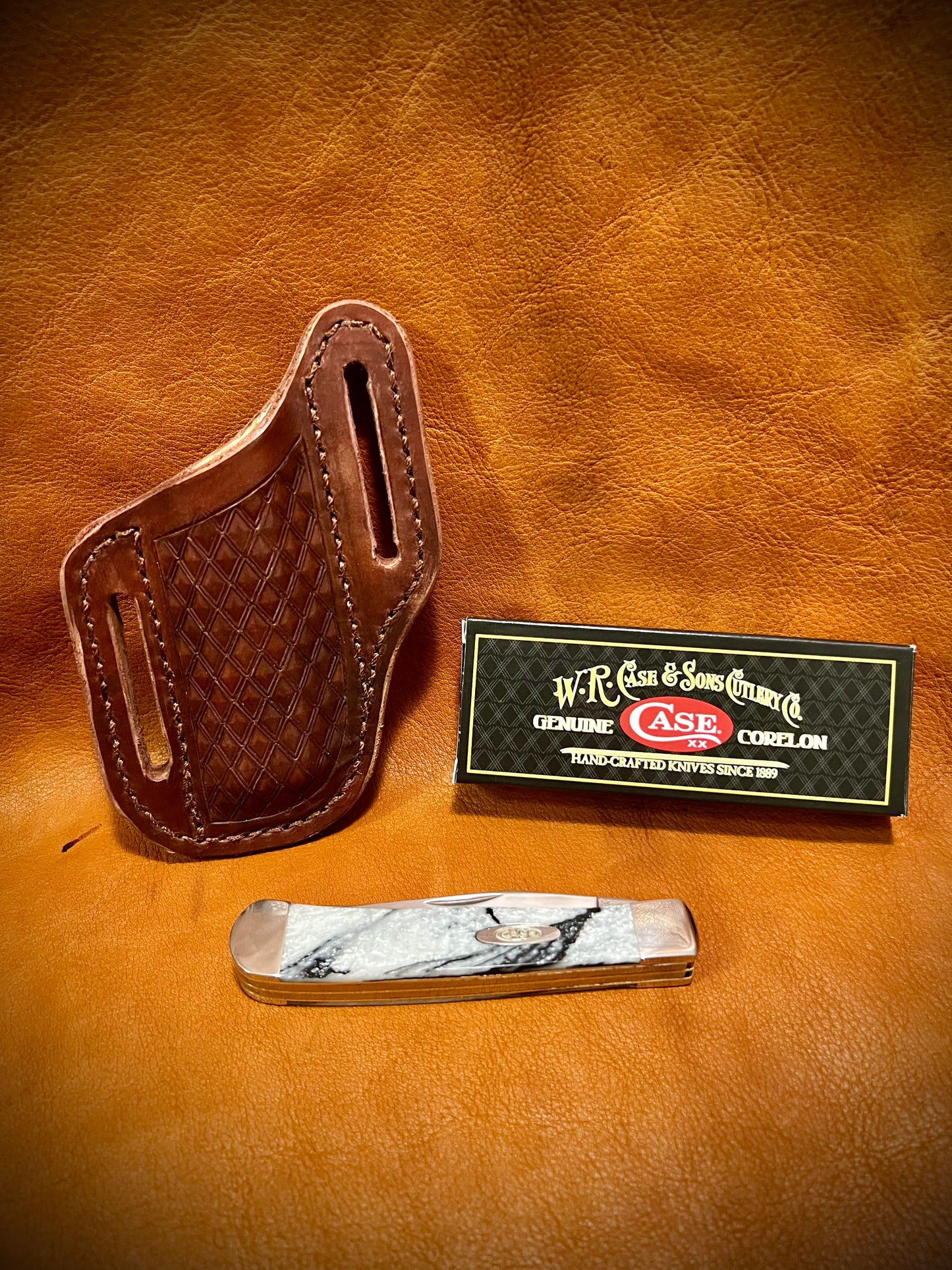 a closed ivory quartz colored case trapper knife with a diamond patterned sheath behind it